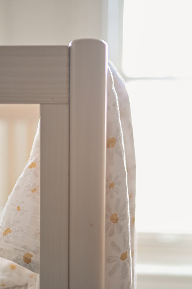 Pehr Daisy Organic Novelty Swaddles hanging over railing of crib. Organic cotton, hand printed. White with daisy pattern.