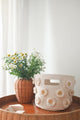 Pehr Daisy Novelty Mini storage bin on table beside potted plant. Screen printed by hand using AZO-Free dyes. Off-white with stitched daisies.