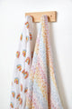 Pehr Rainbows Organic Novelty Swaddles hanging on hook. Organic cotton, hand printed. White with rainbow pattern.