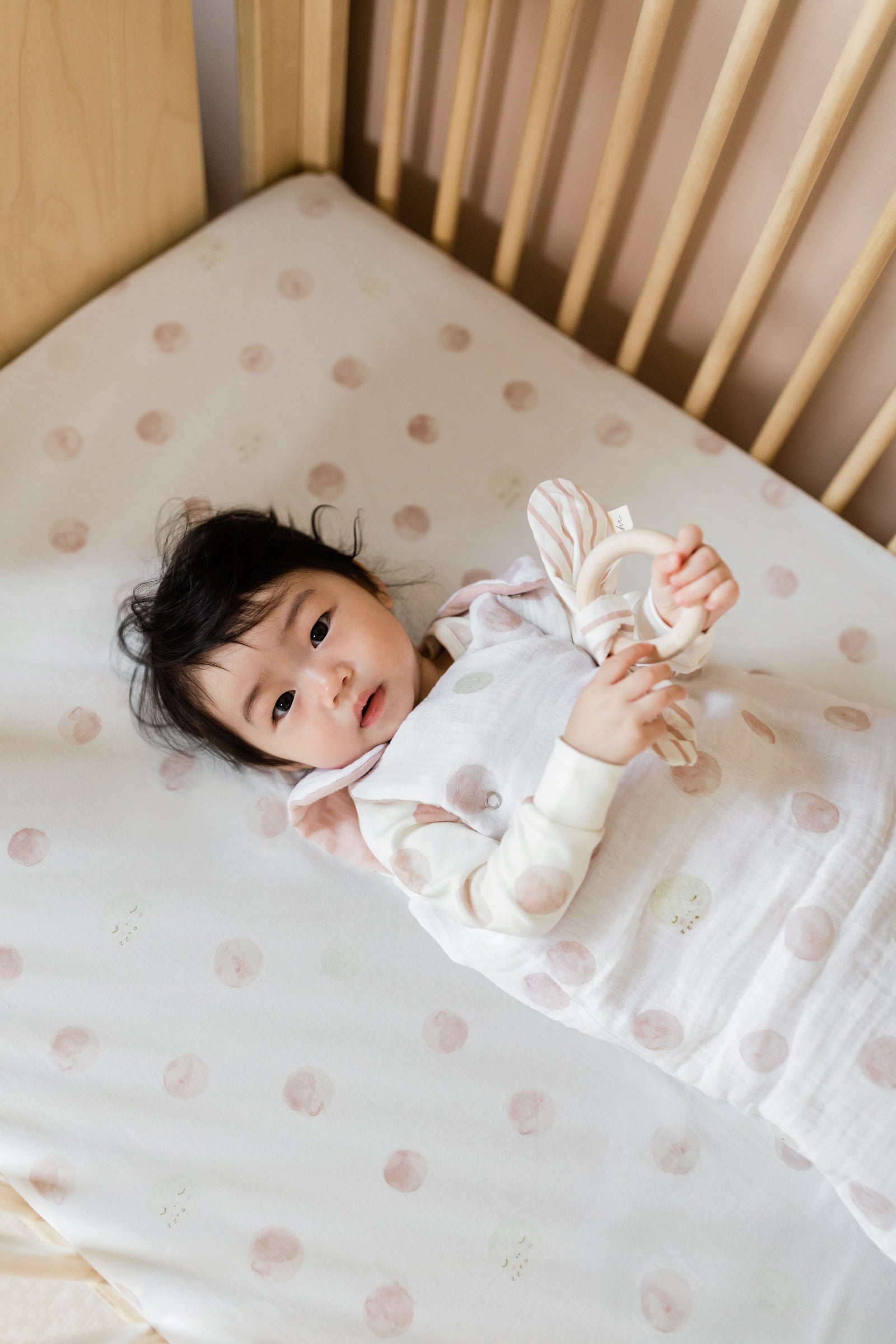 Baby lying in crib holding Teether wearing Dawn Luna Sleep Bag.