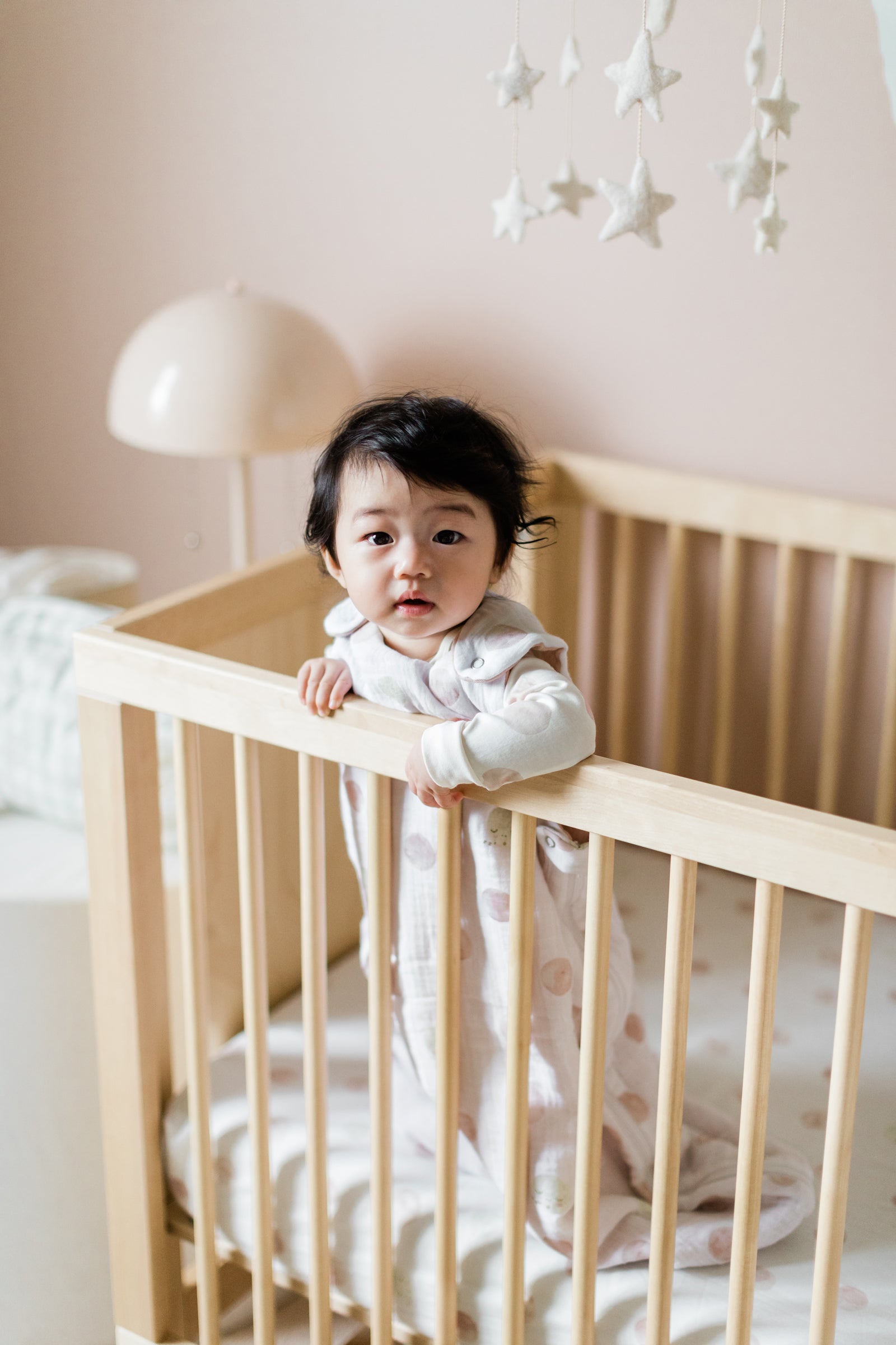 Baby standing in crib wearing Luna Dawn Sleep bag