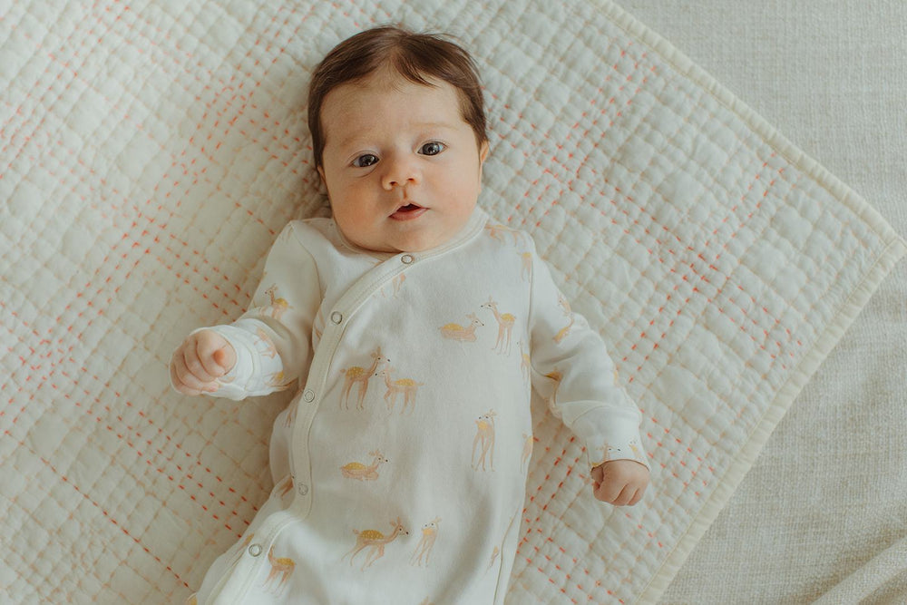 Baby dressed in Kimono Deer Romper laying on pink quilted Lovey Blanket.