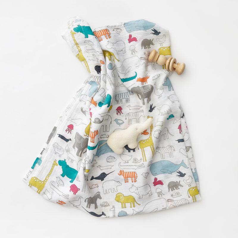 Pehr Rainbows Organic Novelty Swaddles with toy elephant and rattle on top. Organic cotton, hand printed. White with rainbow pattern.