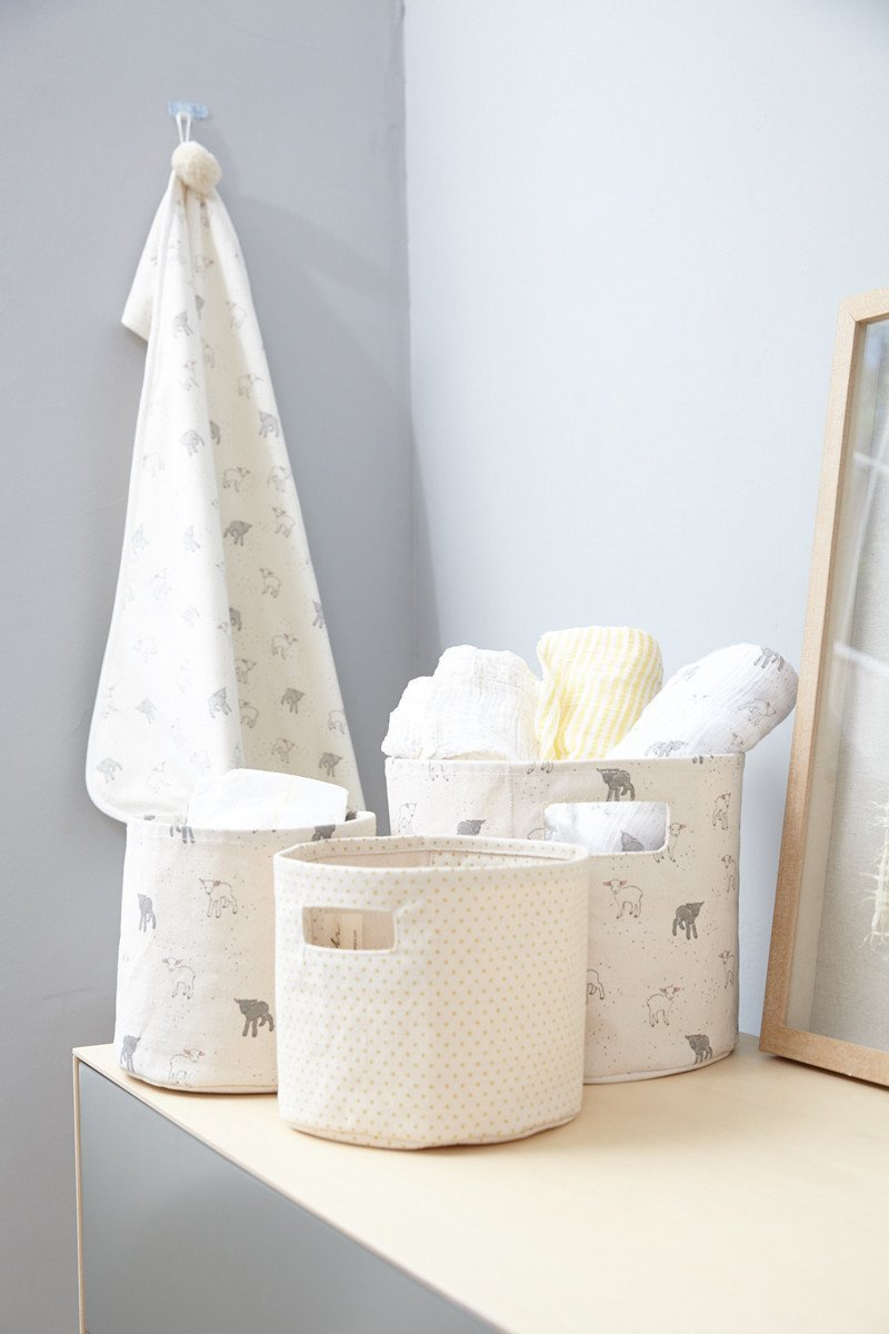 Pehr Little Lamb Organic Novelty Swaddles hanging on wall behind Pehr storage pints and minis. Organic cotton, hand printed. White with little lamb pattern.