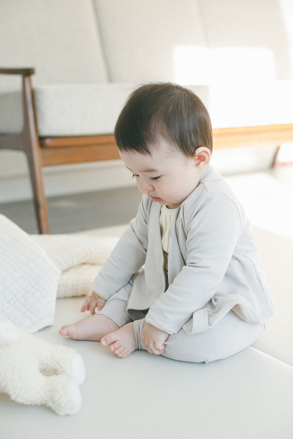 Baby sitting on floor wearing Pehr Dove Grey 3-Piece Set. Organic. Medium grey Pehr Essentials wrap cardigan and Pehr Essentials pant.