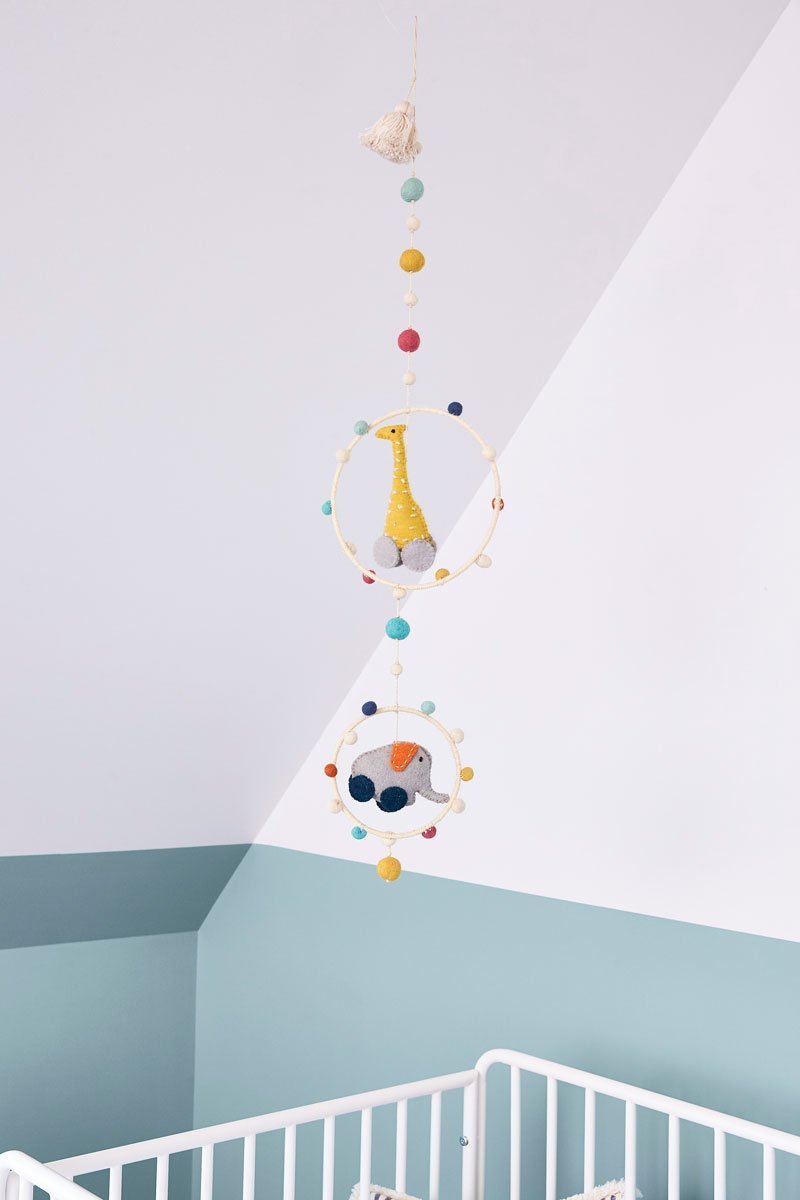 Pehr Pull Toys Hoop Mobile hanging above crib in nursery. Hand made. 100% wool. Giraffe and elephant hanging in hoops with coloured pom poms.