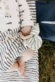 Baby wearing Organic Pehr Stripes Away Bloomers Ink Blue Organic Bloomers & Shorts and holding Pehr Deep Sea On the Go Teether. GOTS Certified Organic Cotton & Dyes. White bow with blue stripes, maple wood ring.