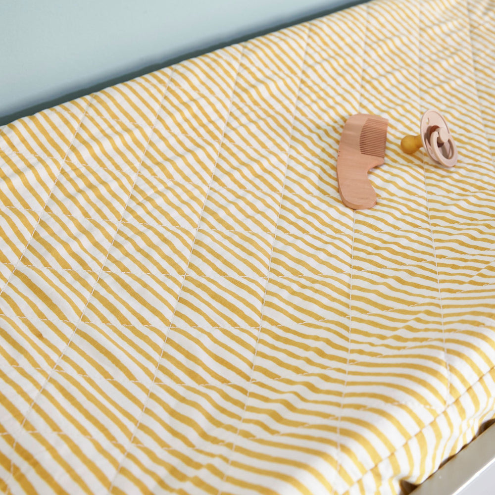 Pehr Stripes Away Marigold Change Pad Cover with comb and pacifier on top. Hand printed. White with gold stripes.