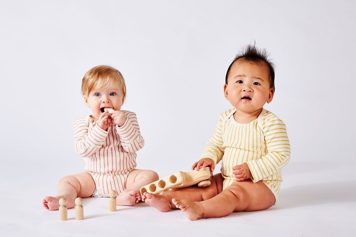 Two babies wearing Pehr Stripes Away Dark Pink and Marigold Organic One-Piece, Long Sleeve. GOTS Certified Organic Cotton & Dyes. White with stripes, long sleeve, button closure at bottom.