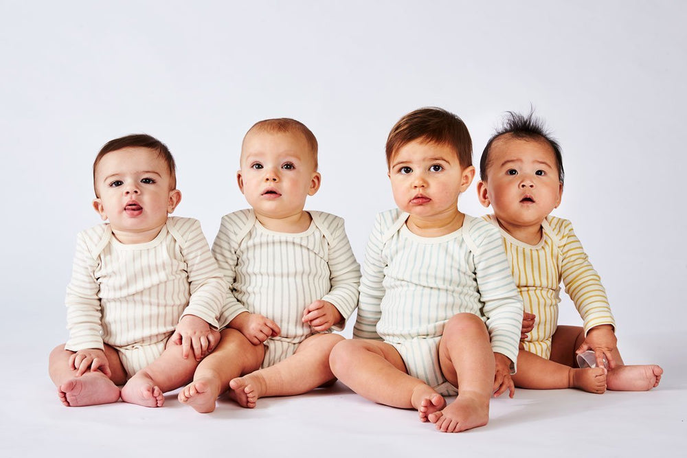 Four babies wearing Pehr Stripes Away Petal, Pebble Grey, Sea, and Marigold Organic One-Piece, Long Sleeve. GOTS Certified Organic Cotton & Dyes. White with stripes, long sleeve, button closure at bottom.