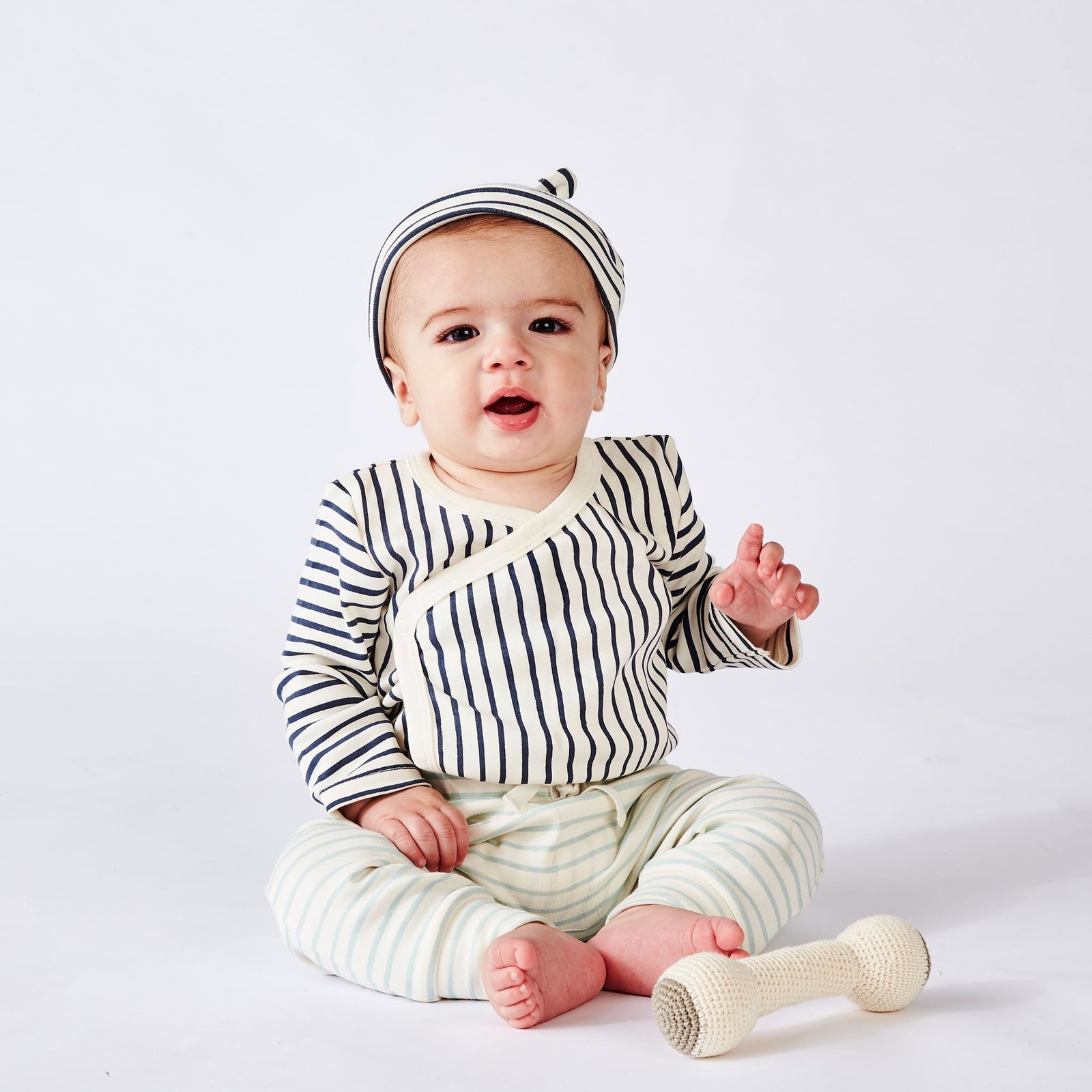 Baby wearing Pehr Stripes Away Ink Blue Organic Kimono One-Piece, Long Sleeve with Pehr Stripes Away Ink Blue Organic Knot Hat and Pehr Sea Organic Harem Pant. GOTS Certified Organic Cotton & Dyes. White with dark blue stripes.