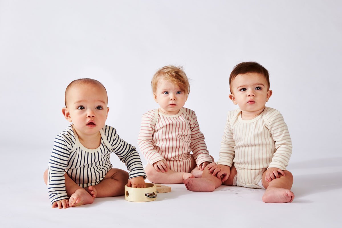 Three babies wearing Pehr Stripes Away Ink Blue, Dark Pink, and Pebble Grey Organic One-Piece, Long Sleeve. GOTS Certified Organic Cotton & Dyes. White with stripes, long sleeve, button closure at bottom.