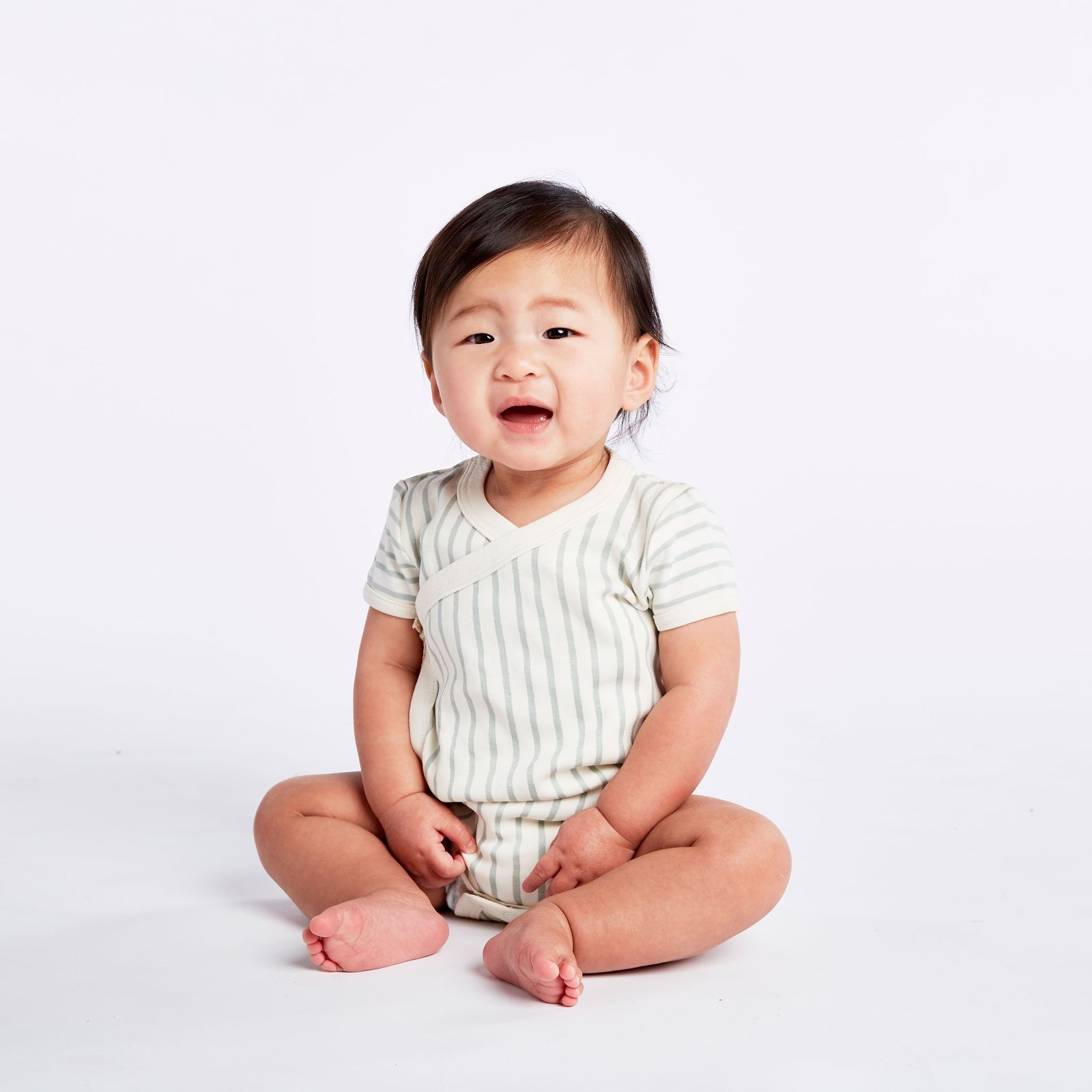 Baby wearing Pehr Stripes Away Sea Organic Kimono One-Piece, Short Sleeve. GOTS Certified Organic Cotton & Dyes. White with light blue stripes.