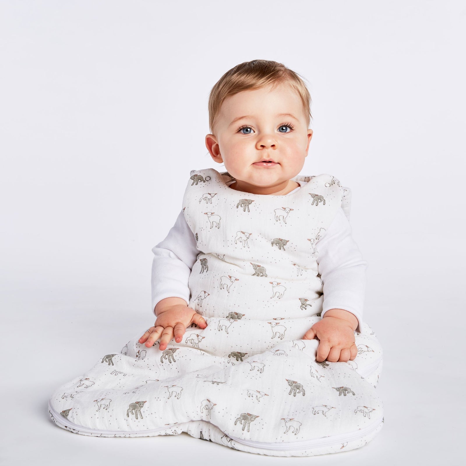 Baby wearing Pehr Little Lamb 1.0 TOG Sleep Bag on white background. 100% organic muslin cotton. White with grey and white little lamb print.
