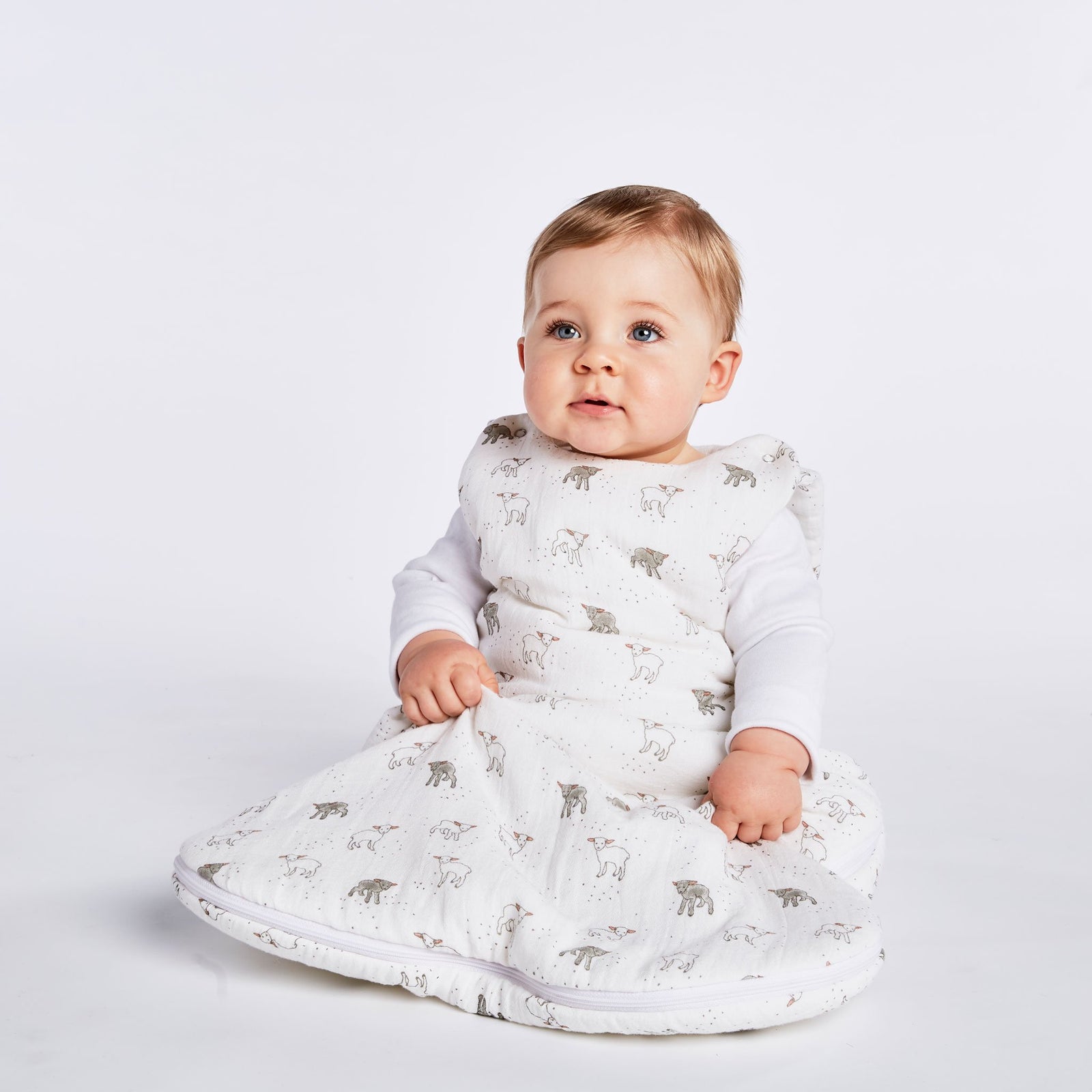 Baby wearing Pehr Little Lamb Organic Muslin 1.7 TOG Sleep Bag over white long sleeve. Organic muslin cotton. White with lamb pattern.