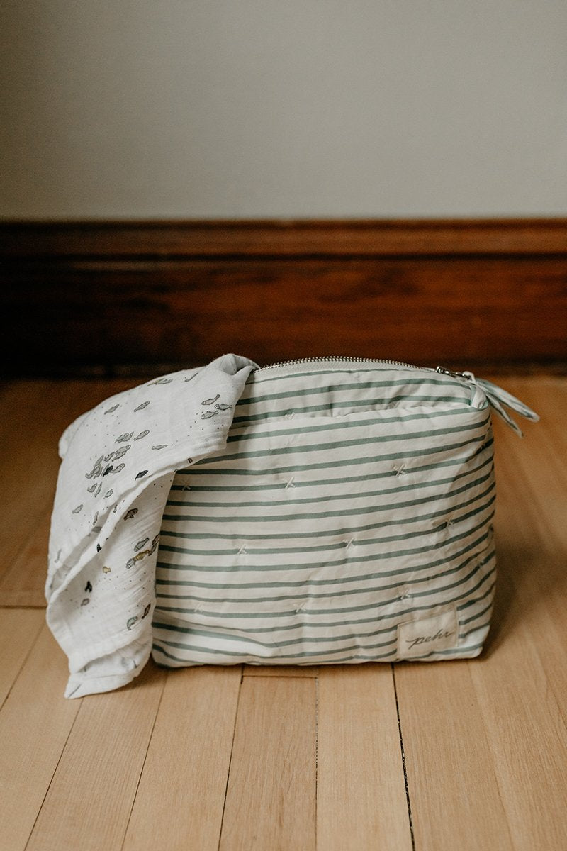 Pehr Deep Sea Organic On The Go Travel Pouch with Pehr Minnow Organic Novelty Swaddles draped over top. GOTS Certified Organic Cotton & Dyes. White with blue stripes and zippered close.